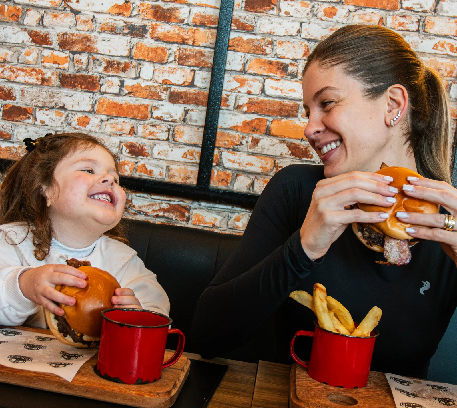 Mãe e filha rindo, cada uma com seu lanche, no salão do Comodoro